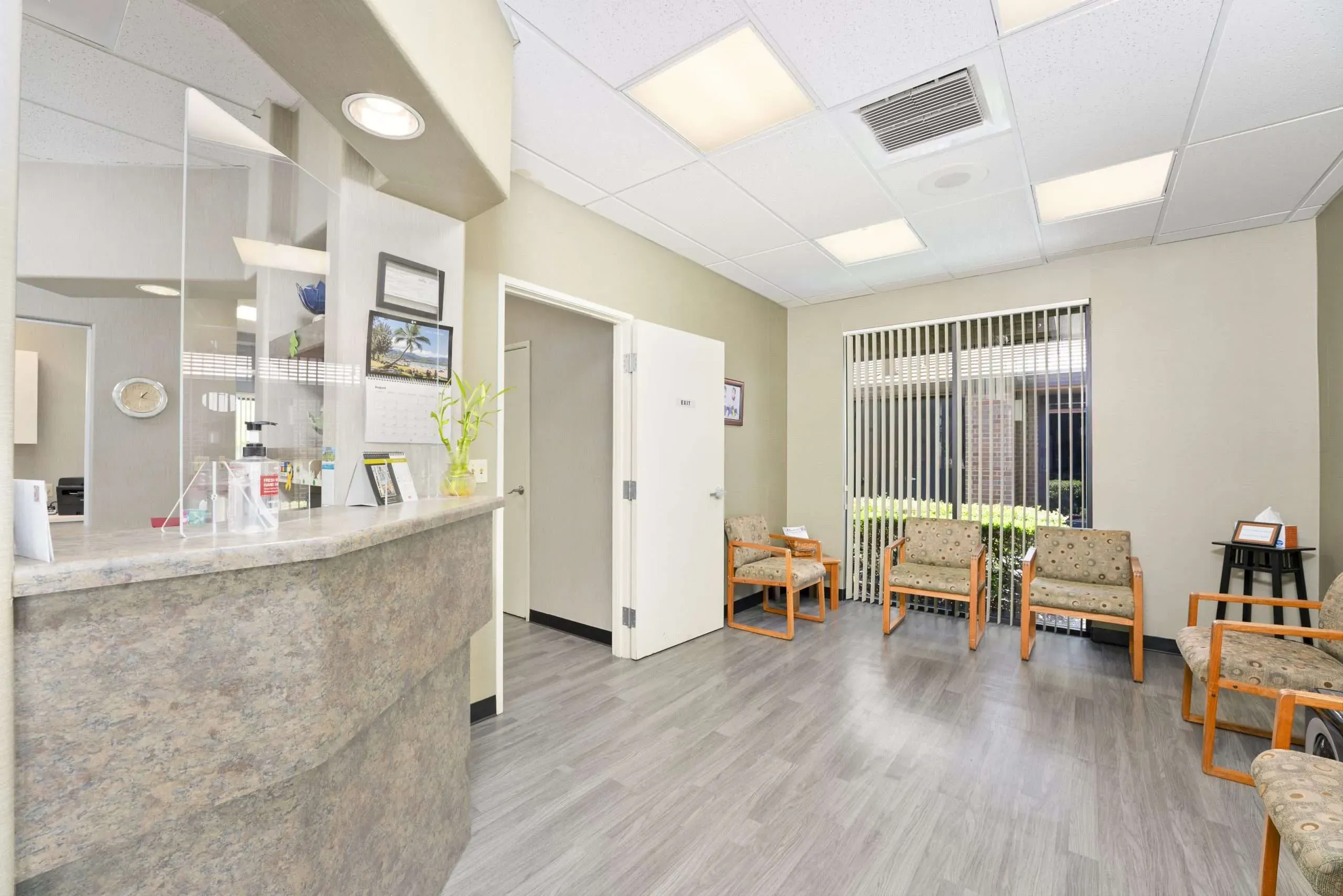 Reception counter and waiting area with wooden armchairs and a window with vertical blinds