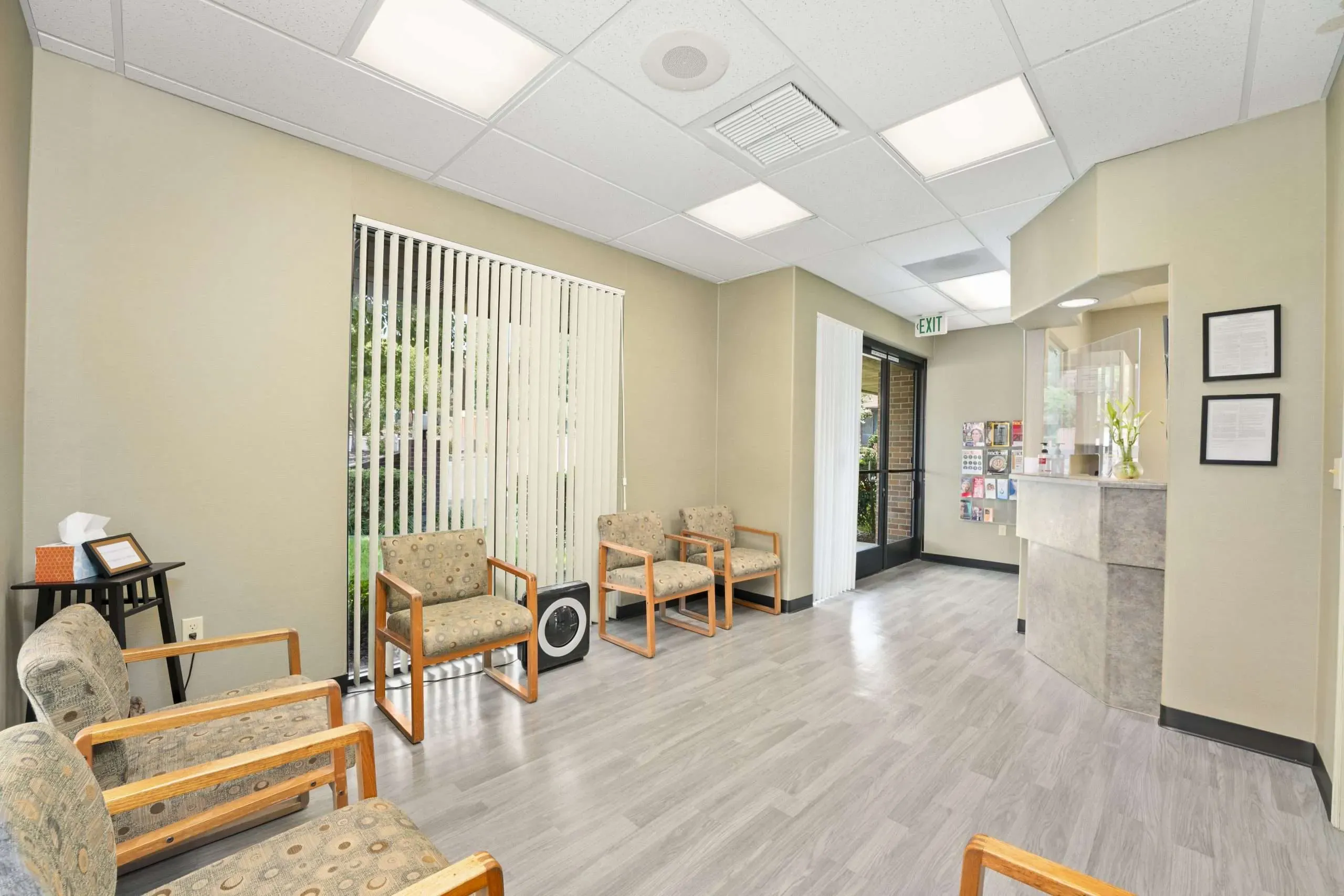 Waiting lounge with upholstered wooden armchairs along the walls and a bright window with vertical blinds